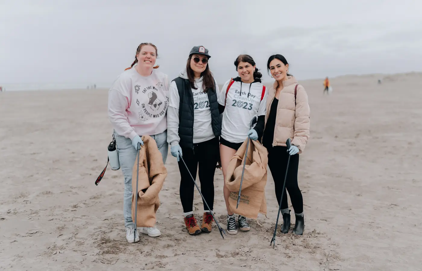 Four student volunteers on a beach holding collection sacks and litter pickers